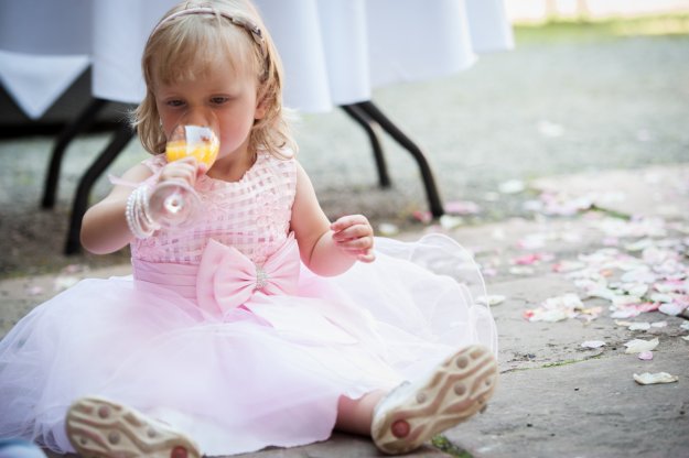 Kind sitzt während einer Hochzeitsfeier auf dem Boden und trinkt